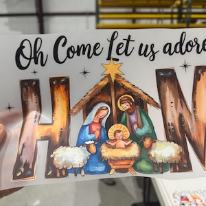 May include: A Christmas graphic featuring the text "Oh Come Let us adore" above a nativity scene. The scene includes Mary, Joseph, baby Jesus, sheep, and a star. The letters "H", "A", and "M" are stylized.