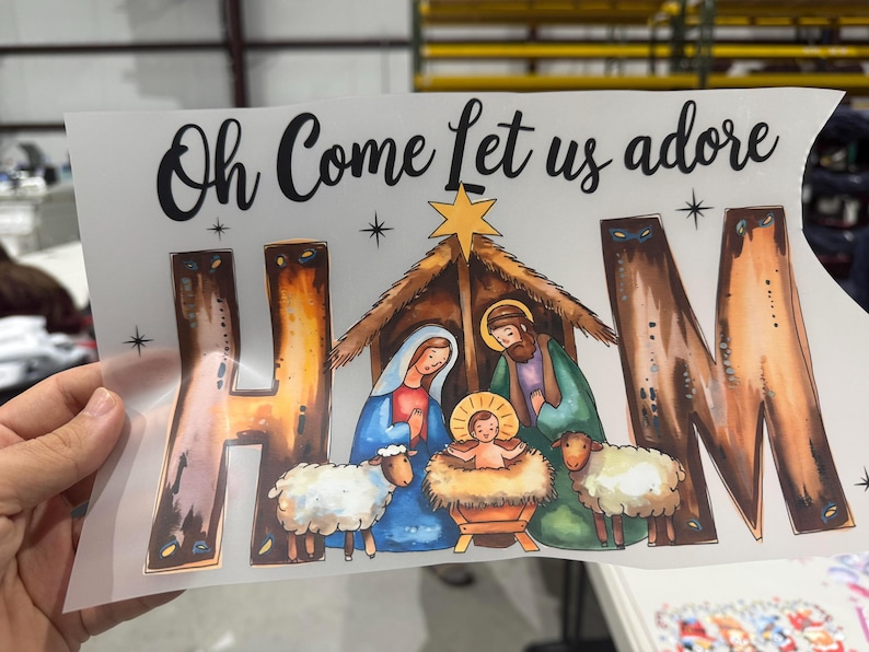 May include: A Christmas graphic featuring the text "Oh Come Let us adore" above a nativity scene. The scene includes Mary, Joseph, baby Jesus, sheep, and a star. The letters "H", "A", and "M" are stylized.
