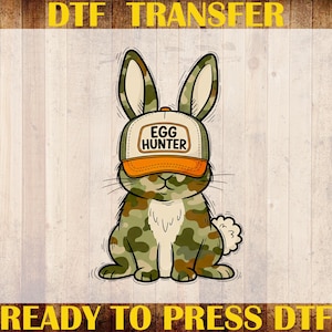 Puede incluir: Un conejo de dibujos animados con una gorra con las palabras "Egg Hunter" en naranja y blanco. El conejo tiene un patr&oacute;n de camuflaje en verde, marr&oacute;n y beige. La imagen es una transferencia DTF con el texto "DTF TRANSFER", "CUSTOM PRINT", "HEAT TRANSFER" y "READY TO PRESS DTF".