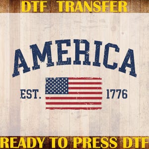 May include: A DTF transfer sheet featuring the word AMERICA in a distressed navy blue font, positioned above a graphic of the United States flag. The text EST. 1776 appears on either side of the flag. The design includes yellow text borders.