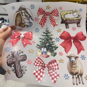 May include: A sheet of Christmas-themed stickers featuring watercolor illustrations. Designs include a nativity scene, bows, a Christmas tree with presents, a cross, a sheep, snowflakes, and stars. The stickers are in various colors, including red, green, and brown.