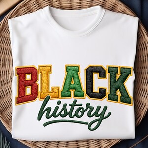 May include: White t-shirt with the embroidered text "BLACK history" in bold, colorful letters. The word "BLACK" is in red, yellow, green, and black, while "history" is in green script. The shirt is displayed on a woven surface.