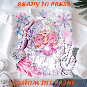 May include: White sweatshirt with a colorful graphic of Santa Claus wearing sunglasses, a disco ball hat, and blowing a bubble. The image includes the text "READY TO PRESS" and "CUSTOM DTF PRINT".