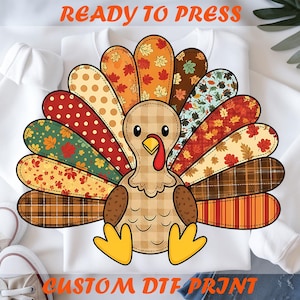 Könnte beinhalten: Weißes Sweatshirt mit einem bunten Truthahn-Motiv. Der Truthahn hat einen karierten Körper und gemusterte Federn in Herbstfarben. Der Text "READY TO PRESS" und "CUSTOM DTF PRINT" sind orange.