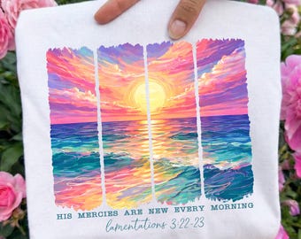 Könnte beinhalten: Weißes Sweatshirt mit einem lebendigen Sonnenuntergang über dem Ozean-Design. Das Kunstwerk enthält Farbtöne von Rosa, Orange, Gelb und Blau. Der Text "HIS MERCIES ARE NEW EVERY MORNING" und "lamentations 3:22-23" ist unter dem Bild aufgedruckt.