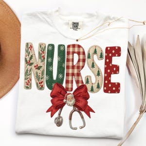 May include: A white t-shirt featuring the word NURSE in large, patterned letters. Each letter has a different holiday design, including holly, snowflakes, red plaid, pine trees, and red polka dots. A red bow with a Santa face and stethoscope.