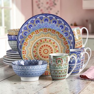 May include: A dinnerware set featuring a large plate, a bowl, and mugs decorated with intricate, colourful mandala-inspired patterns in shades of blue, orange, yellow, and green. The pieces display symmetrical geometric designs and floral motifs.