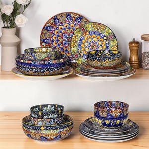 Puede incluir: Un juego de vajilla que incluye platos y cuencos con intrincados y coloridos patrones estilo mandala en tonos azul, amarillo, rojo y verde. La colección incluye platos llanos, platos de ensalada y cuencos apilados con diseños geométricos detallados.