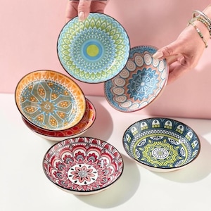 May include: A collection of five small ceramic bowls featuring intricate, colourful mandala-inspired patterns in shades of blue, green, orange, red, and yellow. Each bowl has a distinct geometric design, with some stacked and others displayed separately.