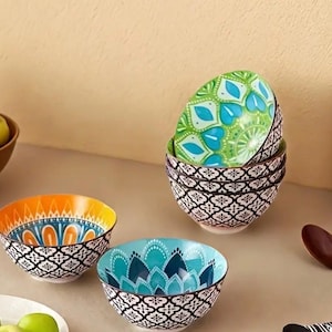 Puede incluir: Colección de cuencos decorativos de cerámica con coloridos estampados florales. Los cuencos presentan un diseño geométrico en blanco y negro en el exterior y diseños interiores vibrantes en tonos naranja, turquesa y verde. Los cuencos están apilados.