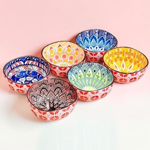 Puede incluir: Un conjunto de cinco cuencos pequeños de cerámica con patrones intrincados y coloridos. Cada cuenco muestra una combinación única de tonos vibrantes que incluyen azul, amarillo, verde y rojo, con diseños geométricos y florales detallados.
