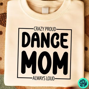 May include: Cream-colored sweatshirt with the text "CRAZY PROUD DANCE MOM ALWAYS LOUD" in a black, bold font. The text is enclosed in a black rectangular frame. The sweatshirt has a crew neck.