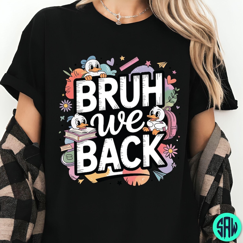 May include: Black t-shirt with the text "BRUH we BACK" in white, featuring cartoon ducks, books, and school supplies. The design includes colourful accents like flowers, hearts, and stars, creating a playful back-to-school theme.