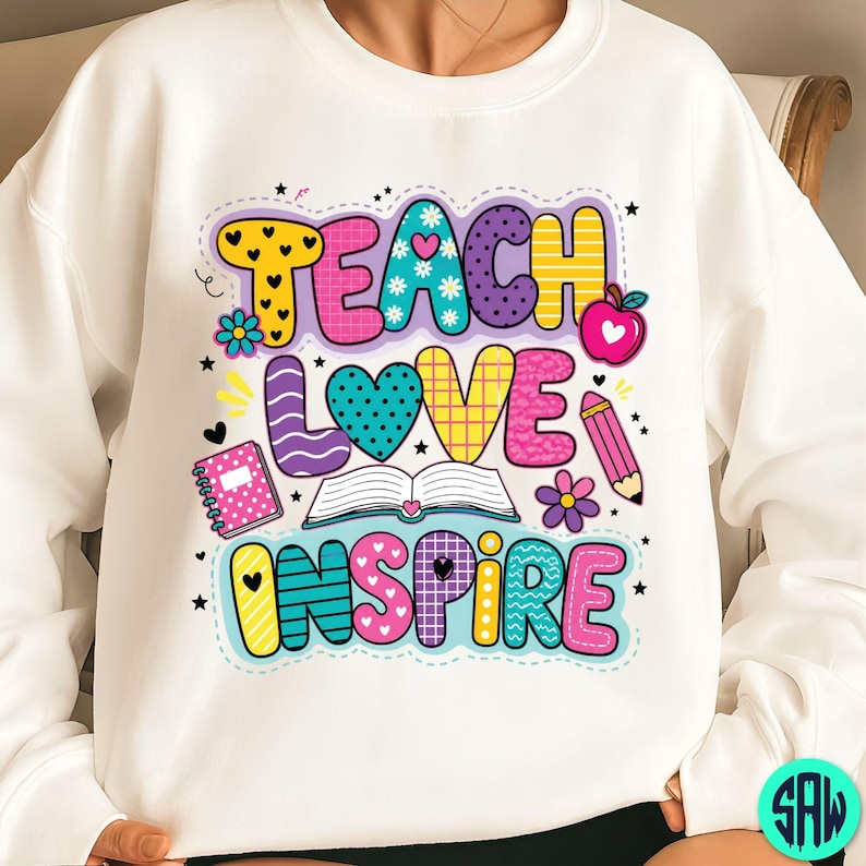 May include: White sweatshirt featuring the words "TEACH LOVE INSPIRE" in a vibrant, cartoonish style. The design incorporates hearts, flowers, an apple, a pencil, and a book, ideal for teachers or those in education.