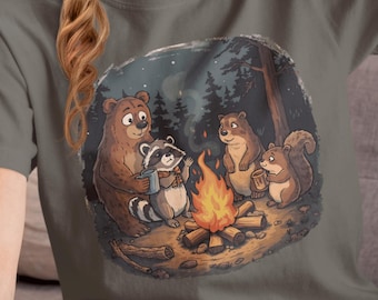 May include: A gray t-shirt featuring a whimsical illustration of woodland animals gathered around a campfire. The design includes a bear, raccoon, chipmunks, and a squirrel, all enjoying the warmth of the fire in a forest setting.