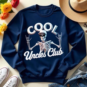 Puede incluir: Sudadera azul marino con un diseño de esqueleto con gafas de sol y gorra, con las palabras "COOL" y "Uncles Club". El esqueleto hace el gesto de la mano de rock and roll.