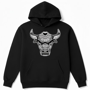 May include: Black hooded sweatshirt featuring a stylized bull head graphic in shades of gray and white. The bull's head has the number 23 on it. The sweatshirt has a front pocket and a hood.