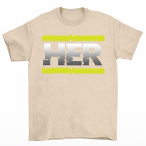 May include: A beige t-shirt featuring the word "HER" in a gradient of gray and white, with a neon green horizontal bar above and below the text. The shirt has short sleeves and a crew neck.