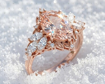May include: An oval-cut peach-coloured gemstone ring set in rose gold. The central stone is flanked by marquise-cut and round-cut clear accent stones arranged in a floral-inspired cluster design along the band, creating a detailed, multi-stone look.