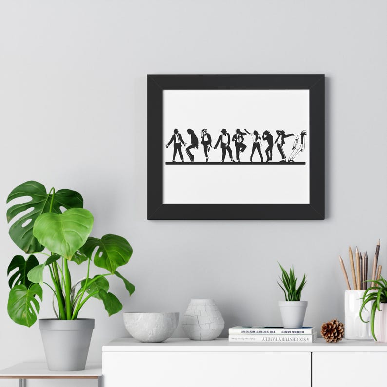 May include: Black framed wall art featuring a line of stylized figures in various dance poses. The figures are in black against a white background. The artwork is displayed on a gray wall, with a green plant and other decorative items in the foreground.