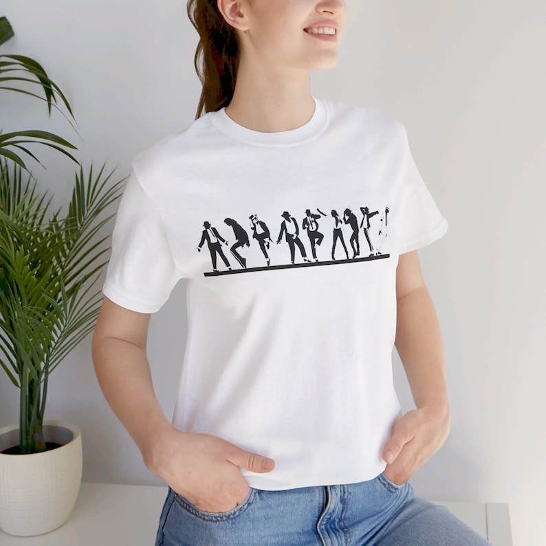 May include: White t-shirt featuring a black silhouette design of a group of people in various poses. The design is printed across the chest. The shirt is made of a soft material and has short sleeves.
