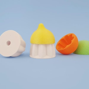 May include: A collection of colorful, whimsical food-shaped erasers. Includes a white cupcake eraser, a lemon-shaped eraser, a halved orange eraser, and a green eraser, all on a light blue background.