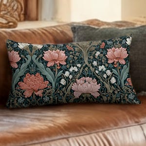 May include: Rectangular cushion with a floral design of pink peonies, white flowers, and green foliage on a dark teal backdrop. The cushion is on a brown leather sofa, with a grey cushion behind it.