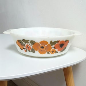 Puede incluir: Fuente ovalada blanca con un estampado floral naranja y marrón. El plato tiene dos asas y está sobre una mesa blanca. El diseño floral incluye flores naranjas con centros oscuros y hojas verdes.