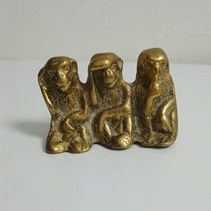 May include: A brass sculpture of the three wise monkeys, each in a different pose. One covers its eyes, another its ears, and the third its mouth. The sculpture is a golden colour and represents the proverb 'See no evil, hear no evil, speak no evil'.
