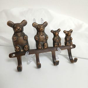以下が含まれることがあります： ブロンズ色の金属製ウォールフック。4匹のクマのフィギュアが特徴です。クマは様々なサイズで、4つのフックが付いた水平バーに取り付けられています。フックは物を掛けるように設計されています。ヴィンテージまたはアンティークな外観です。