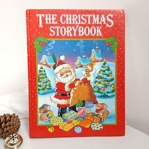 May include: A hardcover book titled The Christmas Storybook with a bright red cover featuring a white-bearded Santa Claus holding a large brown sack, surrounded by decorated Christmas trees, snow-covered houses, a snowman, and small rabbits.