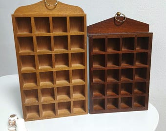May include: Two wooden display shelves with multiple small square compartments. One shelf is light brown, the other is dark brown. Each has a decorative top with a brass ring for hanging. The shelves are empty, ready for displaying small items.