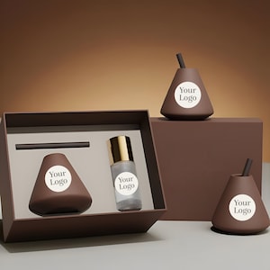 Op de afbeelding: Een bruine geschenkset met een peervormige container, een kleine fles met een gouden dop en twee peervormige objecten. Elk object heeft een witte cirkel met de tekst "Your Logo". De set wordt gepresenteerd op een bruin oppervlak.