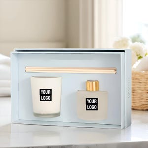以下が含まれることがあります： ライトブルーのボックスに入ったギフトセット。黒い「YOUR LOGO」ラベルが付いた白いキャンドル、金色のキャップと黒い「YOUR LOGO」ラベルが付いたつや消しガラスボトル、木製のディフューザースティックが特徴です。 このセットは、ホームフレグランス用に設計されています。