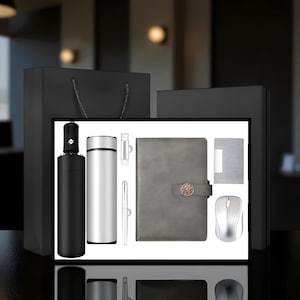May include: A gift set comprising a black umbrella, a silver insulated tumbler, a USB drive, a pen, a grey leather-bound notebook with a gold clasp, a small notepad, and a silver wireless mouse. The items are in a black box.