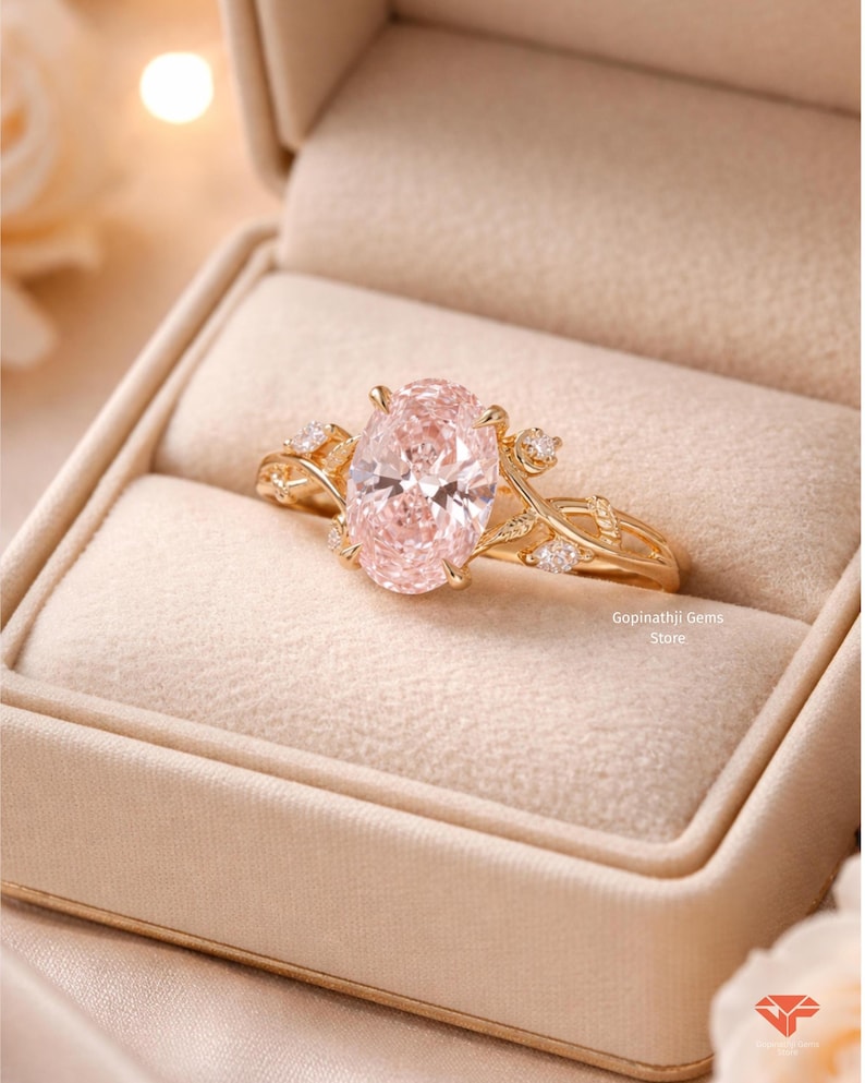 May include: A gold ring with a large, oval-cut pink gemstone, set in a delicate, vine-like design. The ring is displayed in a beige ring box, showcasing the intricate details of the jewelry. The ring is from the Gopinathji Gems Store.