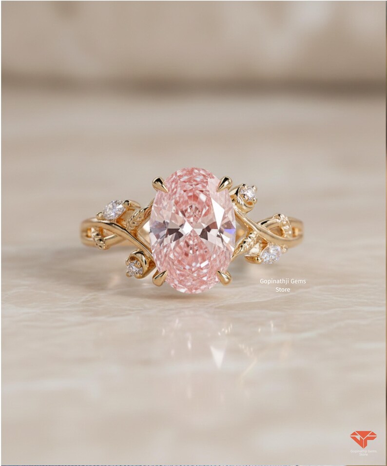 May include: A gold ring featuring an oval, light pink gemstone as the centerpiece. The ring has a floral design with small, clear accent stones. The ring is set on a light-colored surface. The text "Gopinathji Gems Store" is visible.