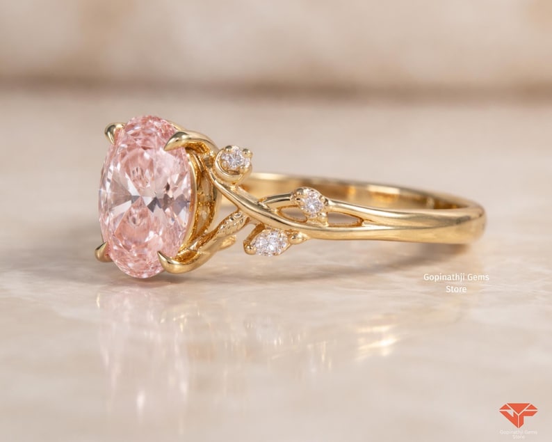 May include: A gold ring featuring a large, oval-cut pink gemstone. The ring has a floral design with small, clear accent stones. The band and floral accents are gold. The ring is displayed on a light-colored surface.