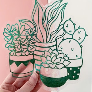 May include: A green iridescent vinyl sticker featuring a group of potted plants. The plants include a succulent, a cactus, and a leafy plant. The pots are decorated with different patterns.