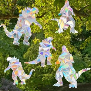 May include: Five iridescent holographic vinyl stickers of Godzilla-like monsters in various poses. The stickers are made of a clear vinyl material with a holographic finish that shimmers in different colours.
