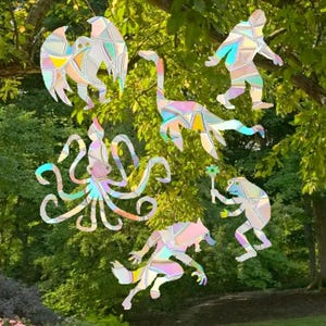 Peut inclure: Un ensemble de six figurines d'animaux en verre teinté iridescent, comprenant un oiseau, un dinosaure, une pieuvre, une grenouille, un loup et un humain. Les figurines sont toutes découpées et ont un reflet arc-en-ciel.