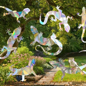 May include: A set of iridescent, stained glass-style gecko stickers. The stickers are in various poses and sizes, and are shown placed on a tree trunk and in a garden setting.