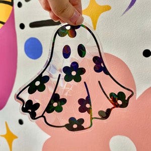 May include: A pink iridescent ghost with black flower accents. The ghost is made of a clear material with a holographic finish.