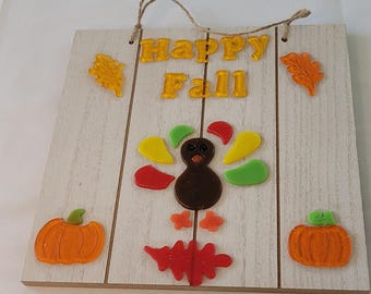 May include: Wooden sign with the words "Happy Fall" in yellow letters. The sign features a turkey, pumpkins, and leaves in shades of orange, yellow, red, and green. A twine loop is attached for hanging.