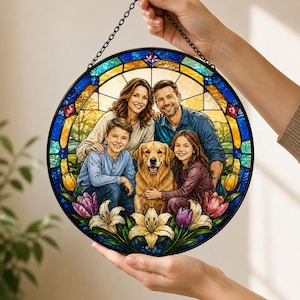 Op de afbeelding: Een rond gebrandschilderd glazen raam met een familieportret met een golden retriever. Het kunstwerk is omlijst met een zwarte rand en een ketting om op te hangen. De afbeelding bevat een kleurrijke bloemenrand met lelies en tulpen.