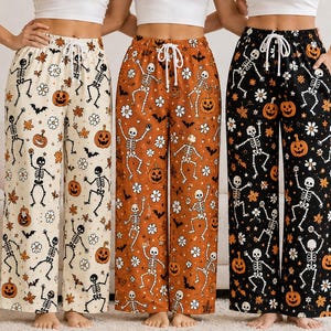 Puede incluir: Tres pantalones de descanso de pierna ancha con un estampado temático de Halloween de esqueletos bailando, calabazas, flores blancas y murciélagos negros. Cada par tiene una cintura elástica con un cordón blanco y bolsillos laterales.