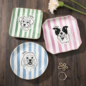 Puede incluir: Tres platos decorativos de cerámica con retratos de perros. Un plato cuadrado con rayas verdes y blancas con un retrato de perro y el nombre "Dolly". Otro plato cuadrado con rayas rosas y blancas con un retrato de perro y el nombre "Coco". Un plato redondo con rayas azules y blancas con un retrato de perro y el nombre "Alex".