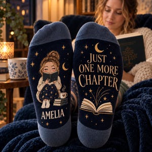 May include: A pair of dark blue socks with light blue cuffs. One sock features an illustration of a person reading a book with the name AMELIA printed below. The other sock displays the text JUST ONE MORE CHAPTER above an open book graphic.