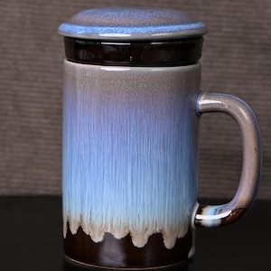 May include: A ceramic mug with a matching lid. The mug features a gradient design, transitioning from a dark brown base to a light blue top. The handle and lid have a similar color scheme. This mug is suitable for hot beverages.