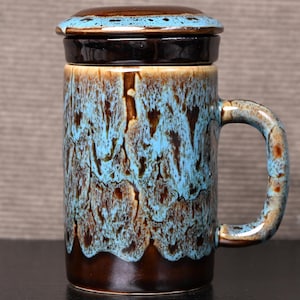 Peut inclure: Une tasse en céramique avec un couvercle, présentant un glaçage marron et bleu. La tasse a une anse et une forme cylindrique. Le couvercle est également marron et bleu. La tasse mesure environ 13 cm de haut.